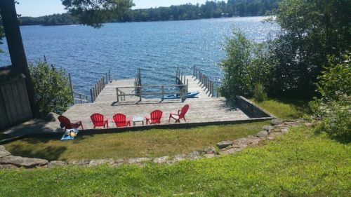 a photo of a dock overlooking a lake with adirondack chairs