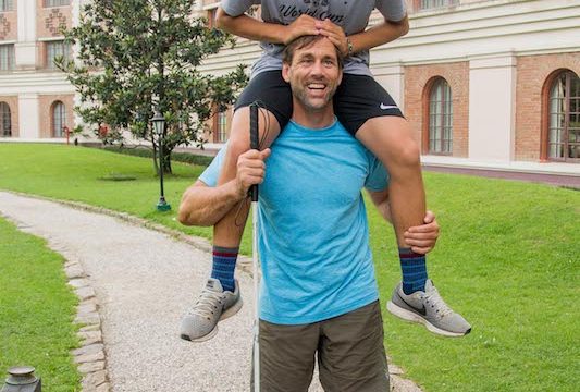 a photo of erik weihenmayer with his son arjun on his shoulders as a teenager