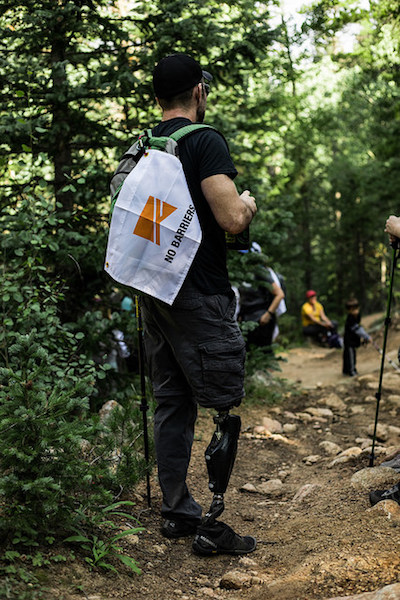 a photo of an amputee standing on the trail with a no barriers flag on his pack 2018