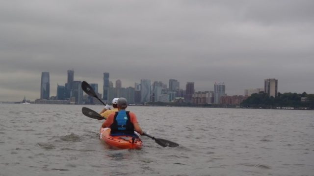 a photo of erik weihenmayer kayaking around nyc with new jersey on his right and statue of liberty up ahead