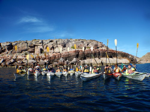 a group shot of everyone in kayaks with paddles raised