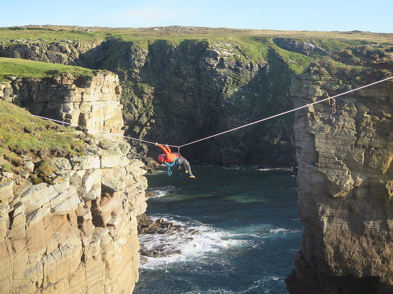 Erik Tyrolean traverses from Yesnaby Castle sea stack back to the mainland, positioned high in the air to avoid battling the raging current below. Credit: Mick Tighe 