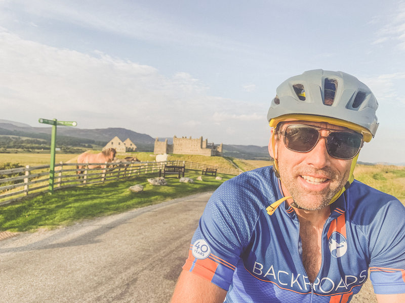 A close-up of Erik on the bike smiling with castles and countryside in the background