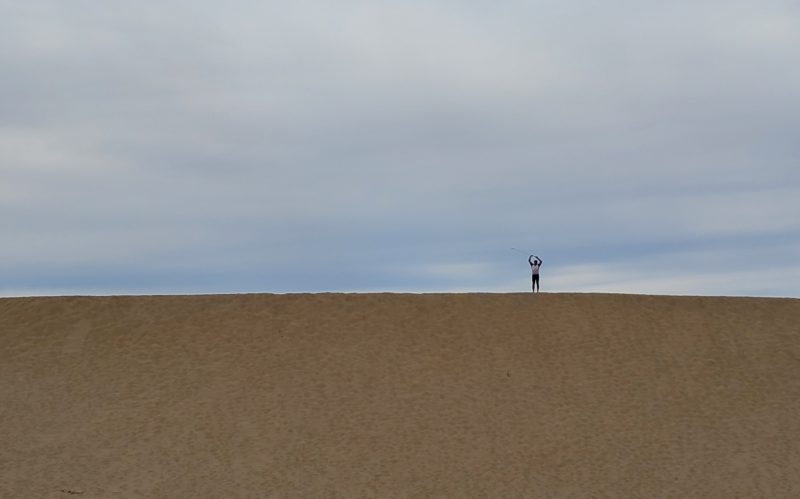 Erik waving his arms from the top of a dune, dwarfed by the scale of the sand piled up.