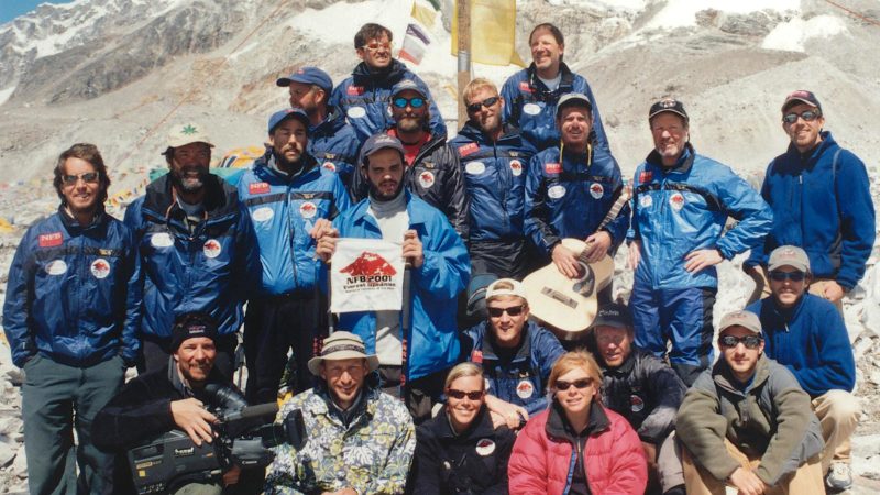 Erik Weihenmayer and 19 Everest team members taking a group photo at the basecamp holding a National Federation of the Blind flag. 