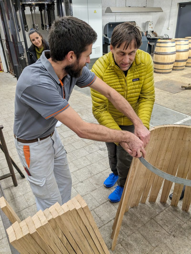 A cooper guides Erik's hands over a barrel they are making for the day.