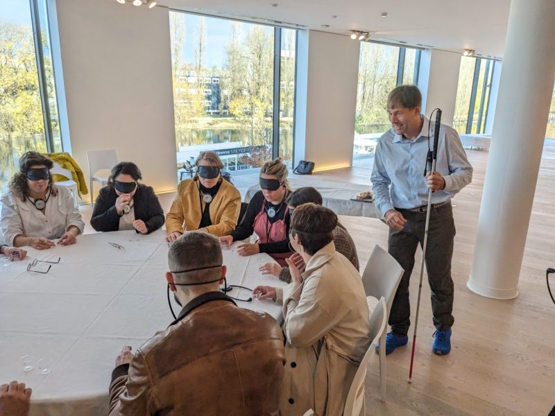 Erik walking around a table of managers blindfolded as they explore using all their other senses to experience the world around them.